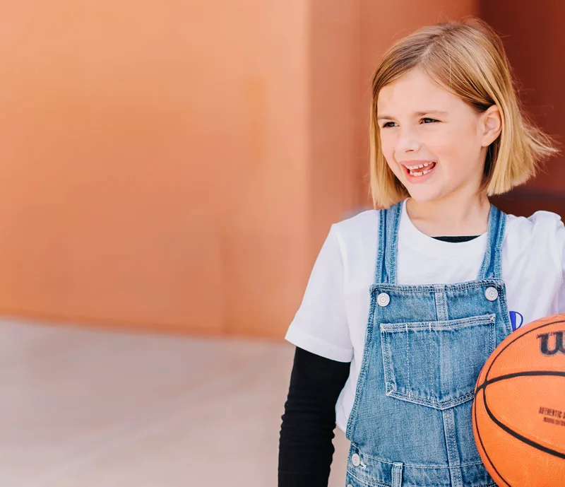Smiling girl holding a basketball at a Bay Club camp