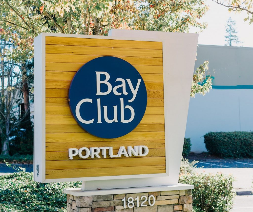 Welcome! We hope you enjoy your visit. Wooden corner sign with Bay Club Portland logo.